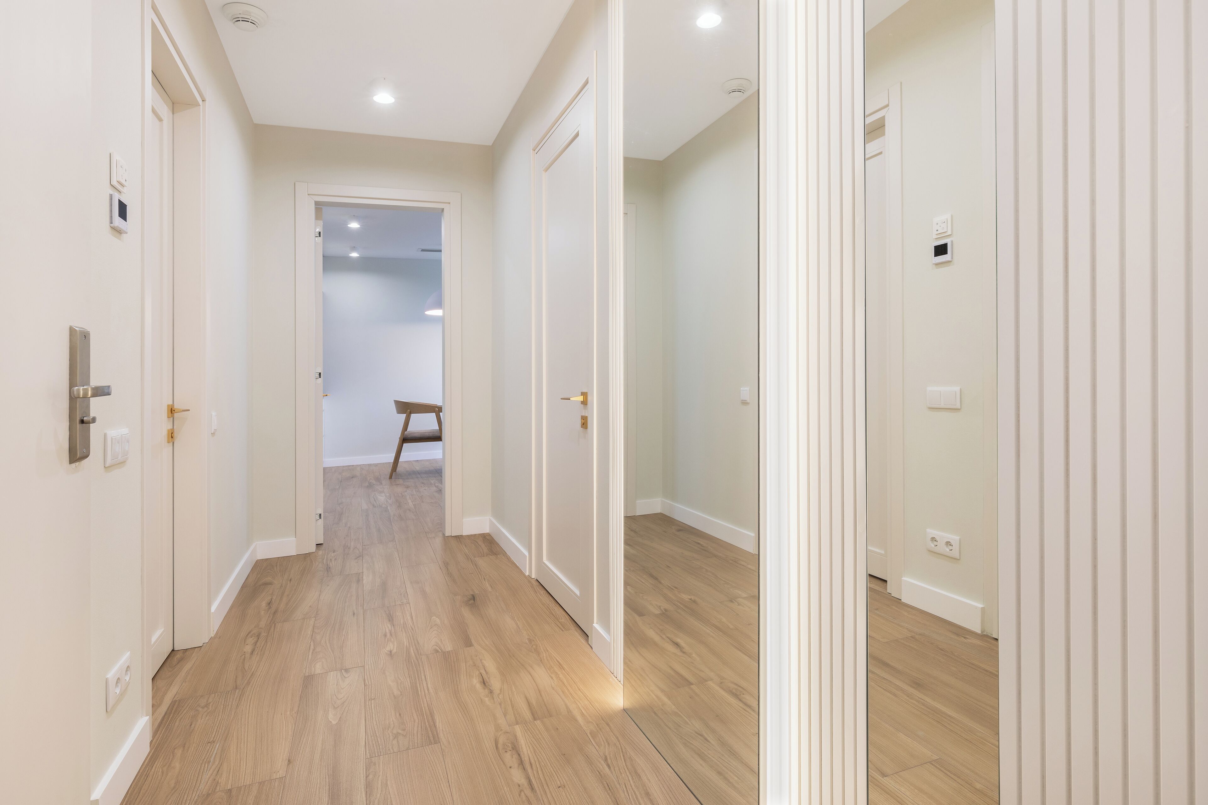 Un pasillo con piso de madera, paredes blancas y puertas que dan a otras habitaciones.