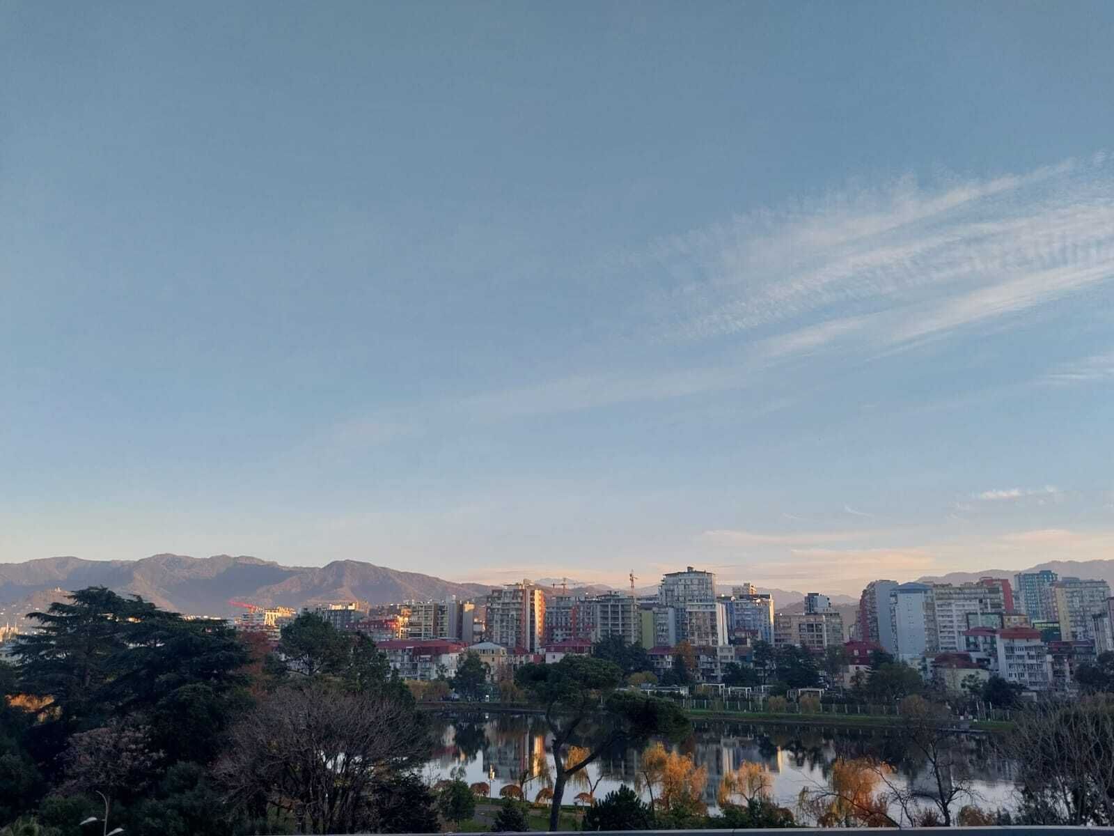 Un paisaje urbano con una masa de agua que refleja edificios y montañas al fondo.