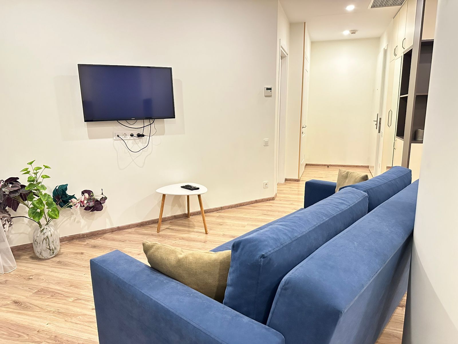 Un soggiorno moderno con un divano blu capiente, un tavolino bianco e una televisione a schermo piatto fissata al muro.