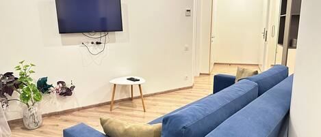 Un soggiorno moderno con un divano blu capiente, un tavolino bianco e una televisione a schermo piatto fissata al muro.