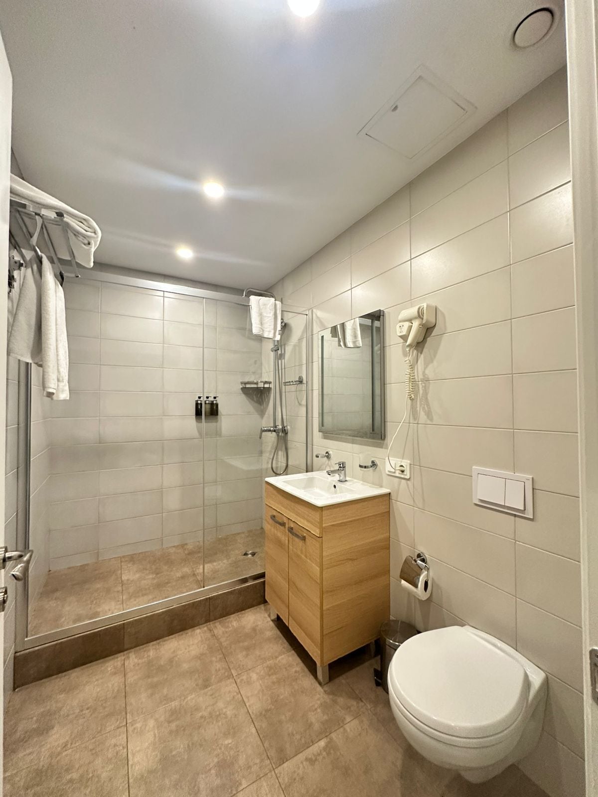 A modern bathroom with a glass shower enclosure, a wooden vanity, a white toilet, and a towel rack.