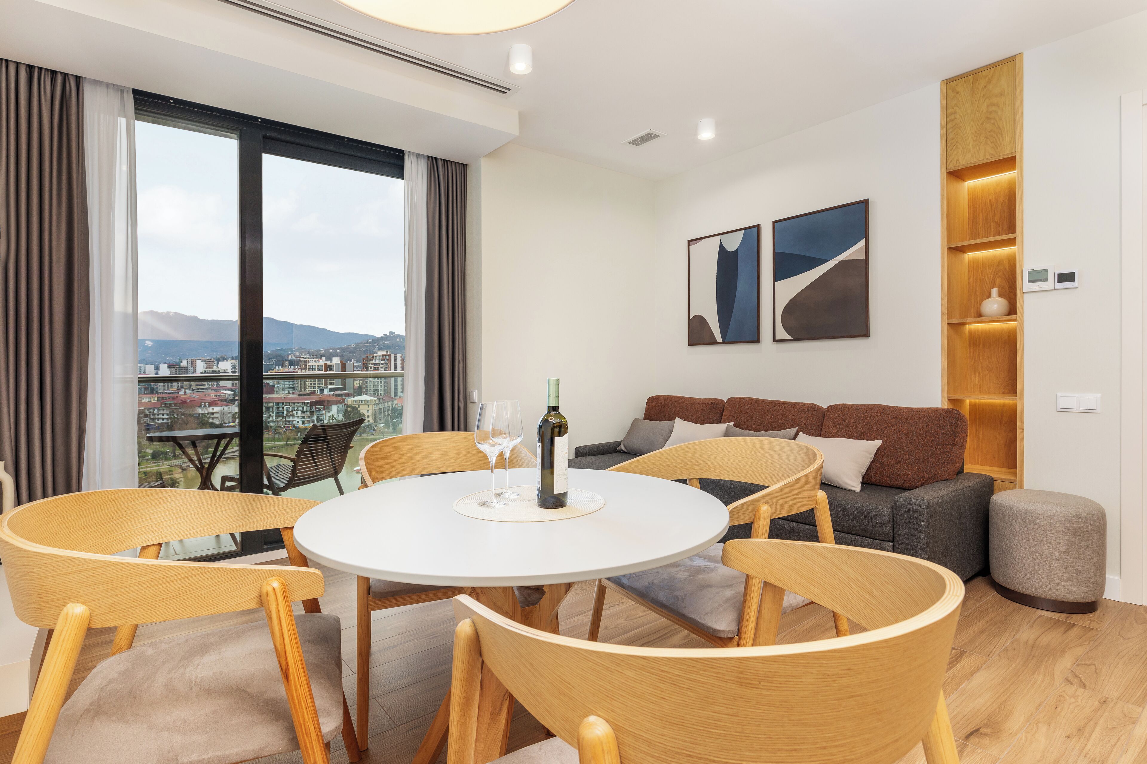 A modern hotel room with a dining area, a sofa, and a view of the city.