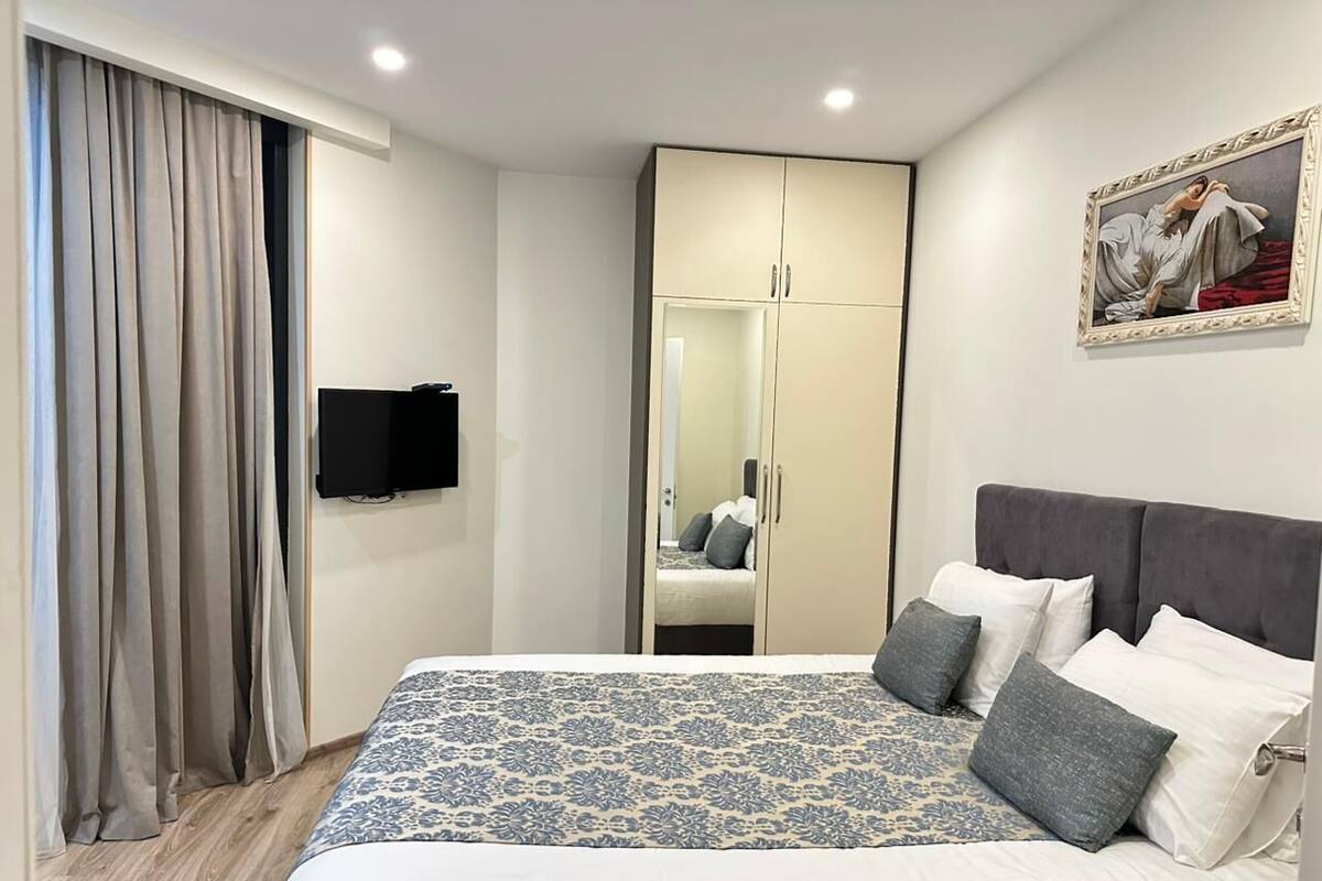 A neatly arranged bedroom with a bed, a wardrobe, a television, and a painting on the wall.