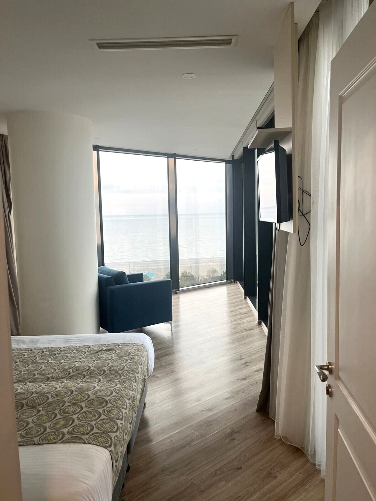 A hotel room with a large bed, a sofa, a TV, and a view of the sea.