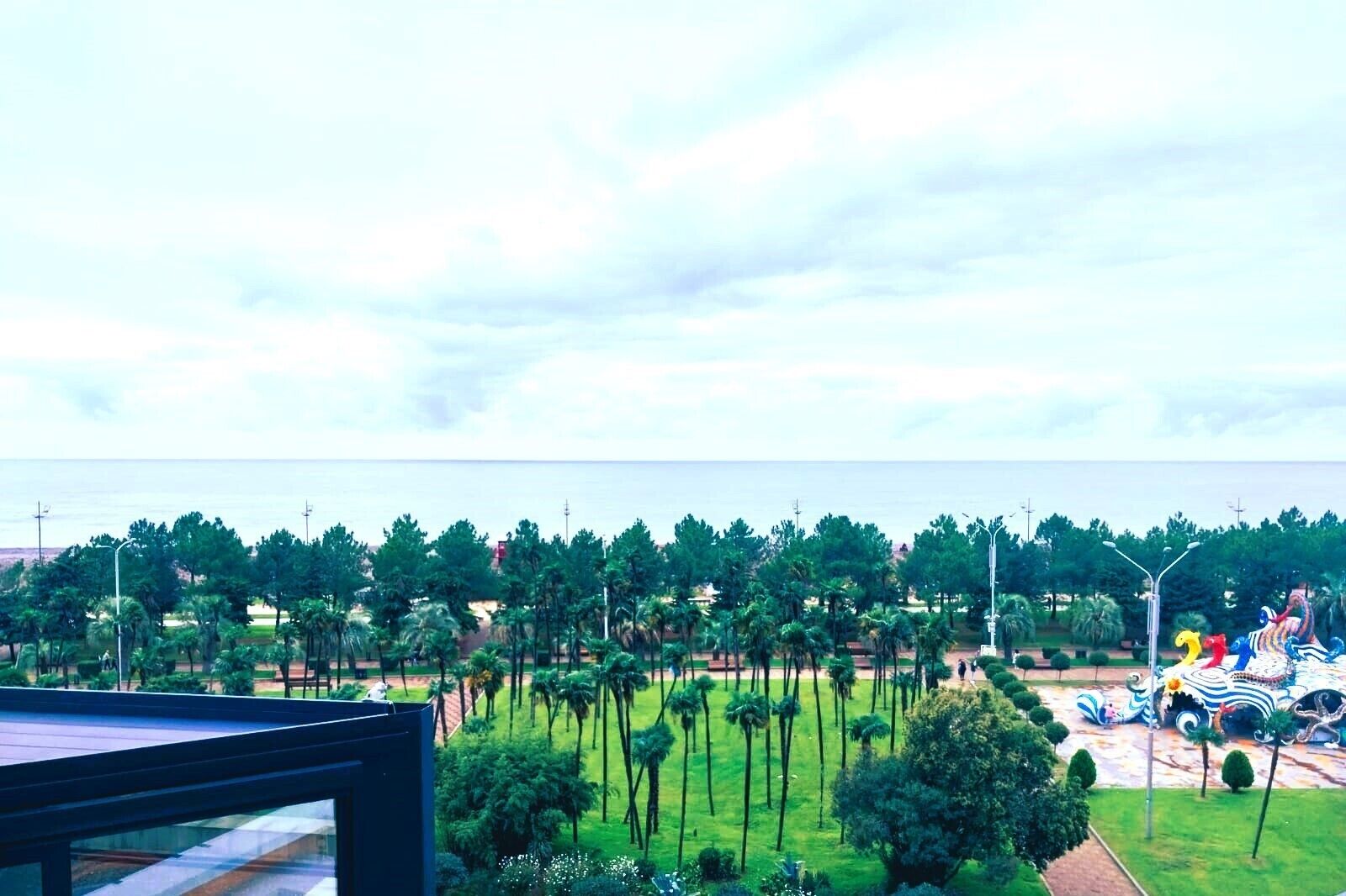 Vista de una zona ajardinada con palmeras y una escultura colorida.