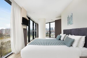Un dormitorio moderno con una cama grande, vistas a la ciudad y un televisor de pantalla plana.