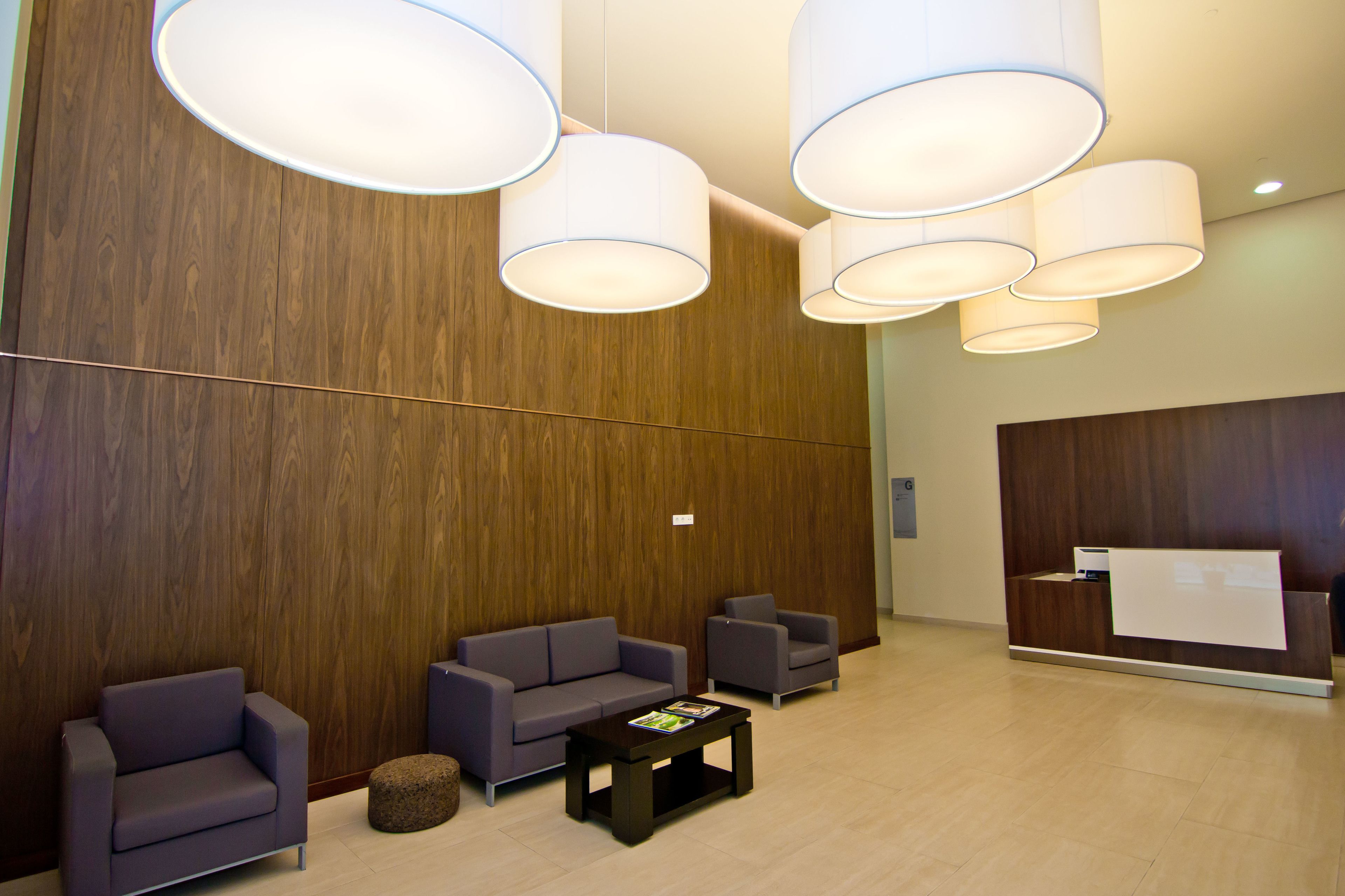 A modern lobby with a wooden reception desk, two sofas, a coffee table, and large pendant lights.