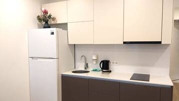 A compact kitchen with a white refrigerator, a sink, a coffee maker, and a small countertop.