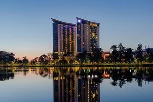 Un hotel moderno de gran altura, ubicado a orillas de un lago tranquilo cuyas aguas reflejan el edificio y los árboles circundantes.