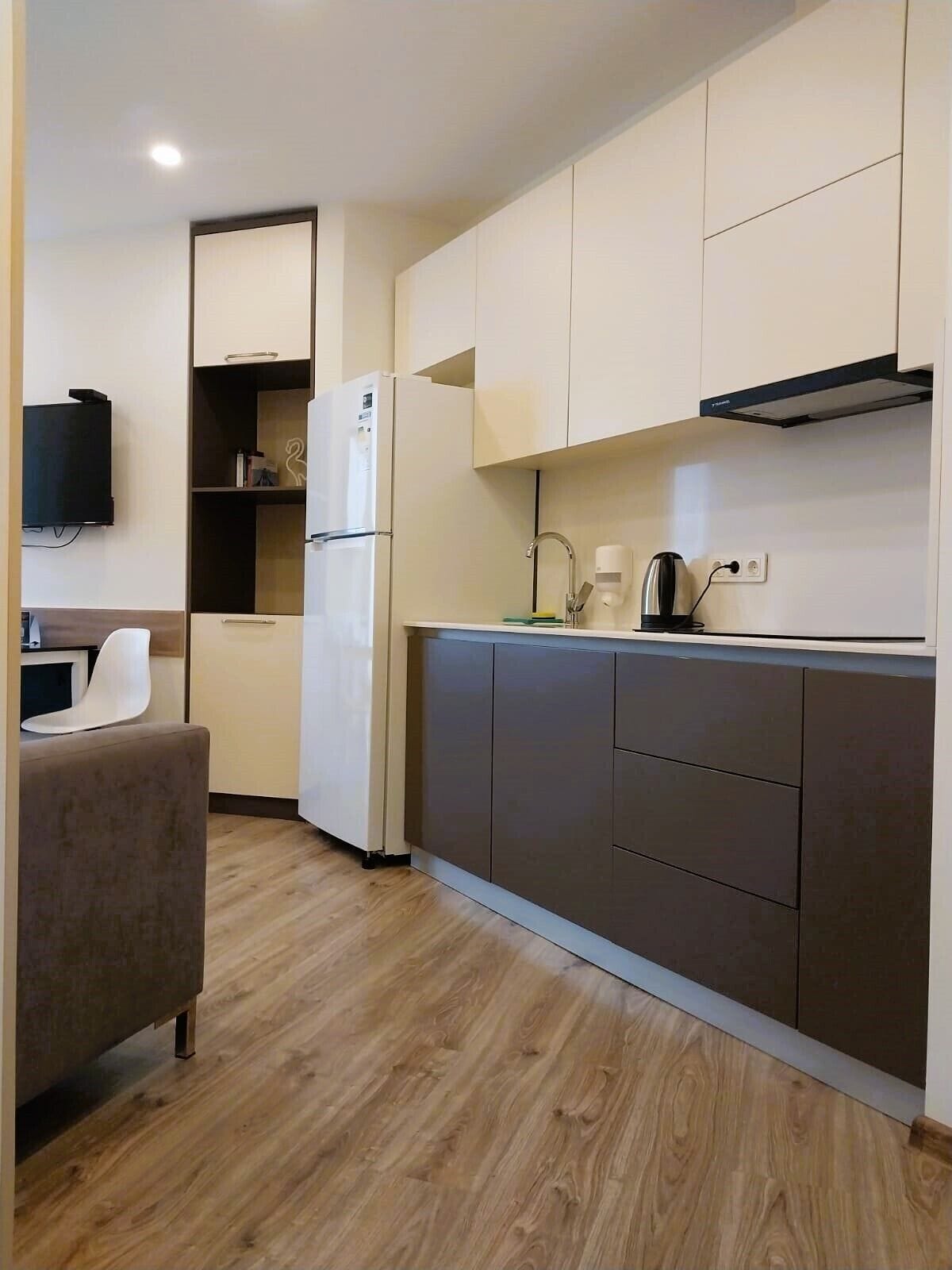 A compact kitchen with modern appliances, a built-in oven, a coffee maker, and a flat-screen TV mounted on the wall.
