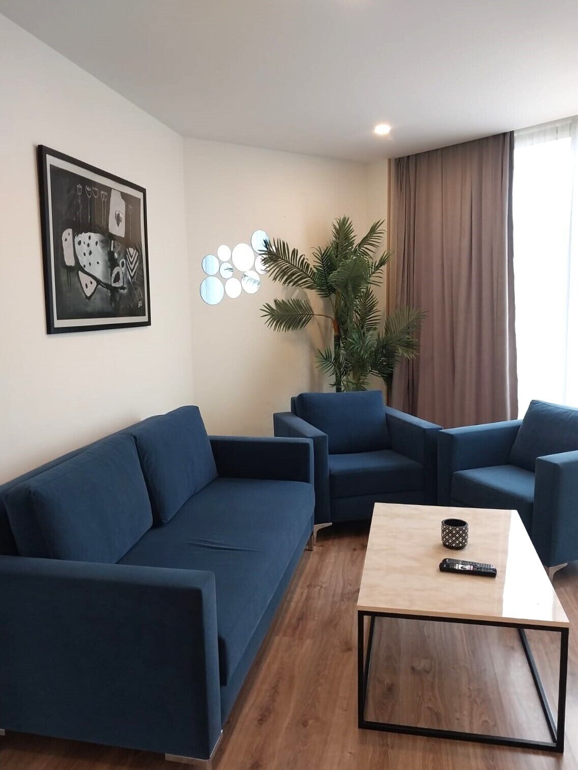 Una sala de estar moderna con un sofá azul, dos sillones, una mesa de centro, una planta en maceta y una obra de arte enmarcada en la pared.