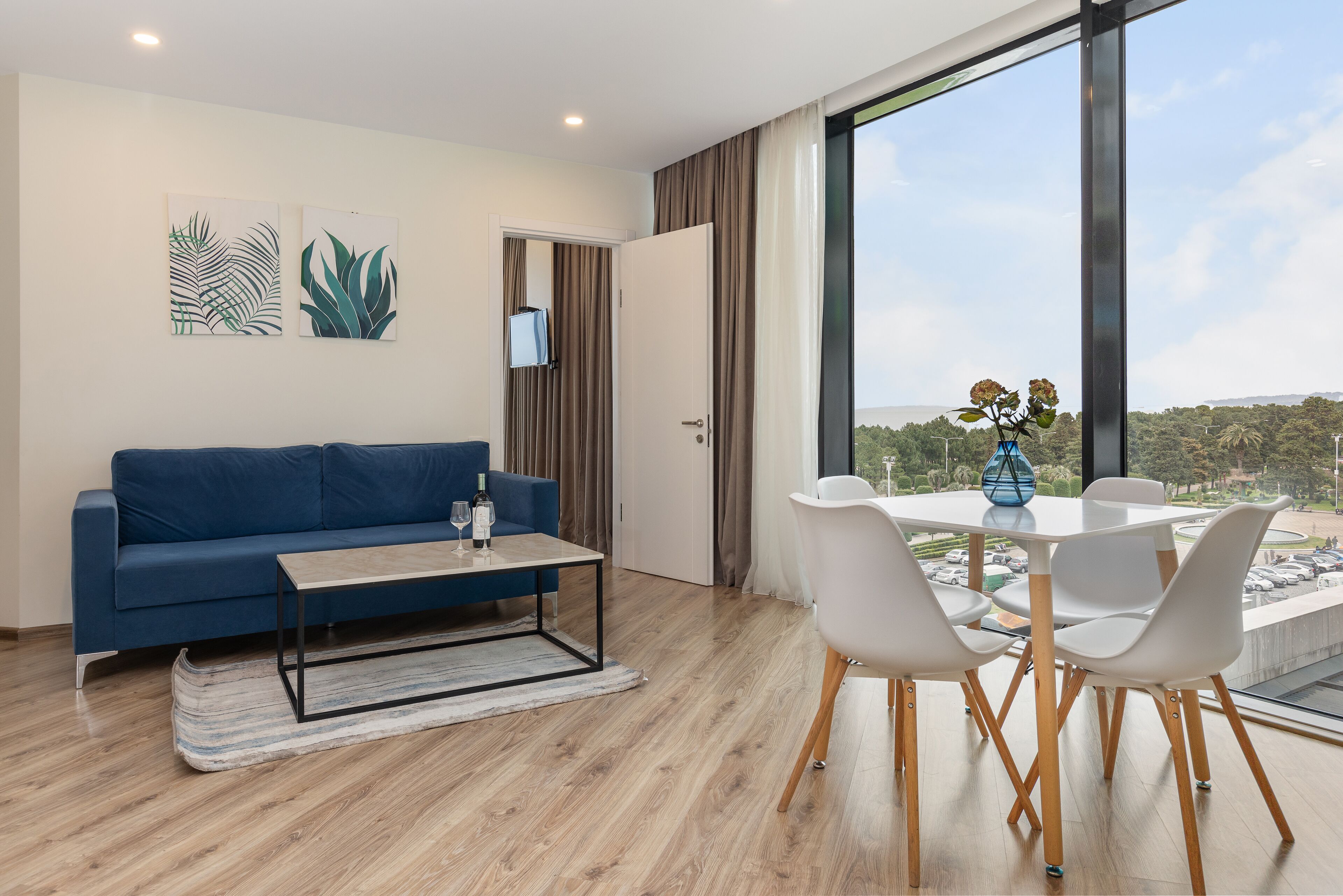 A modern living room with a blue sofa, a coffee table, and a dining area with white chairs.