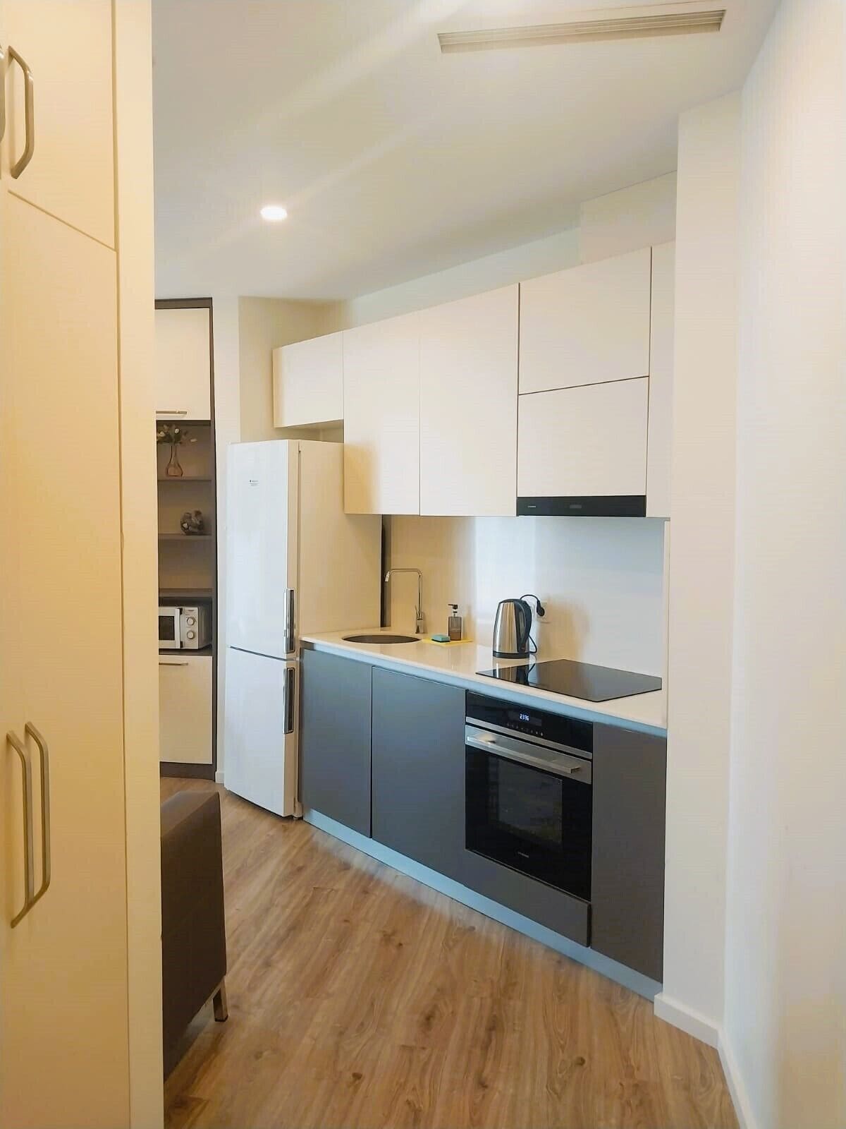 A compact kitchen with white cabinets, a built-in oven, and a microwave.