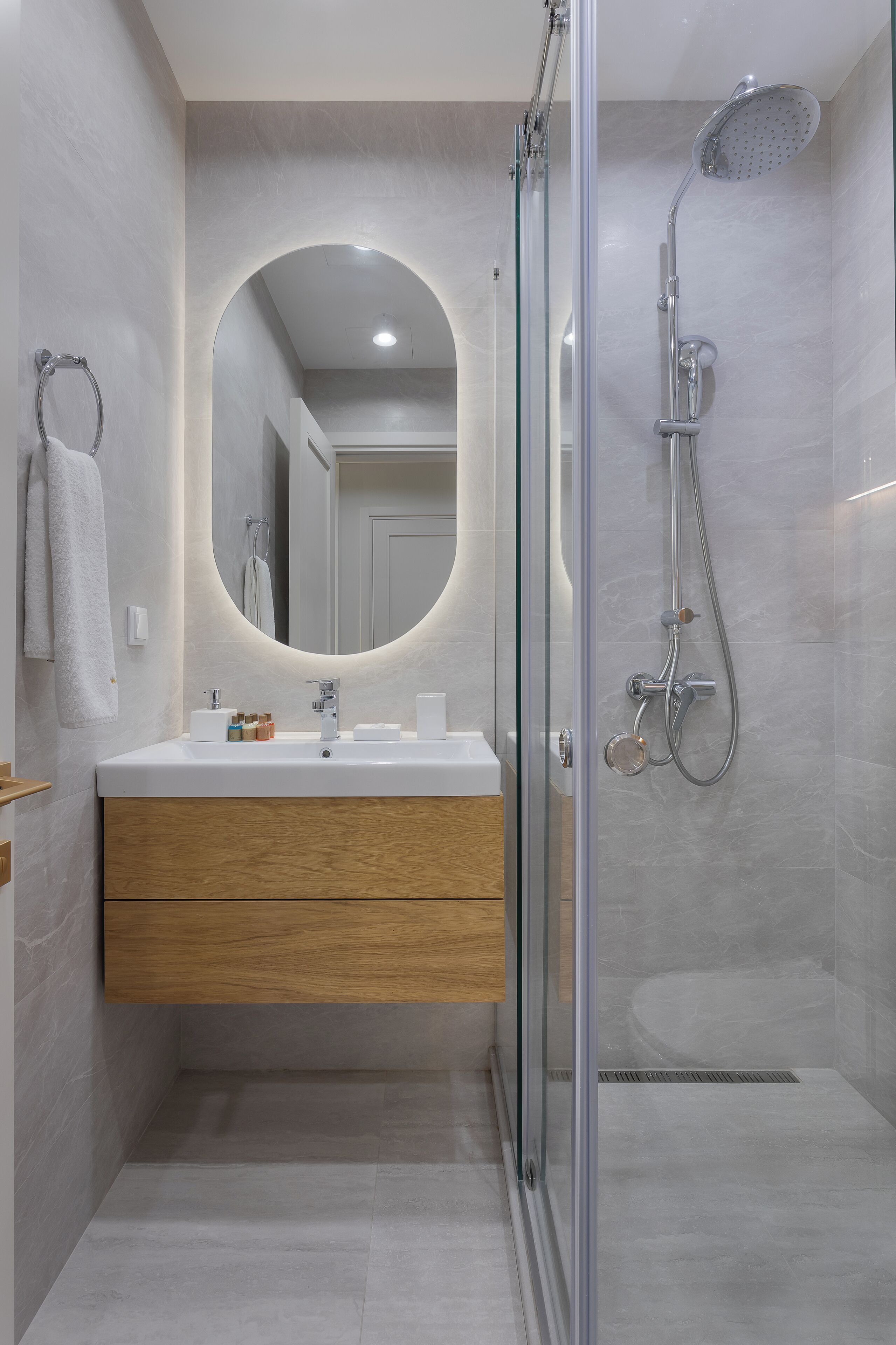 A modern bathroom with a glass shower enclosure, a wooden vanity, and a large mirror.