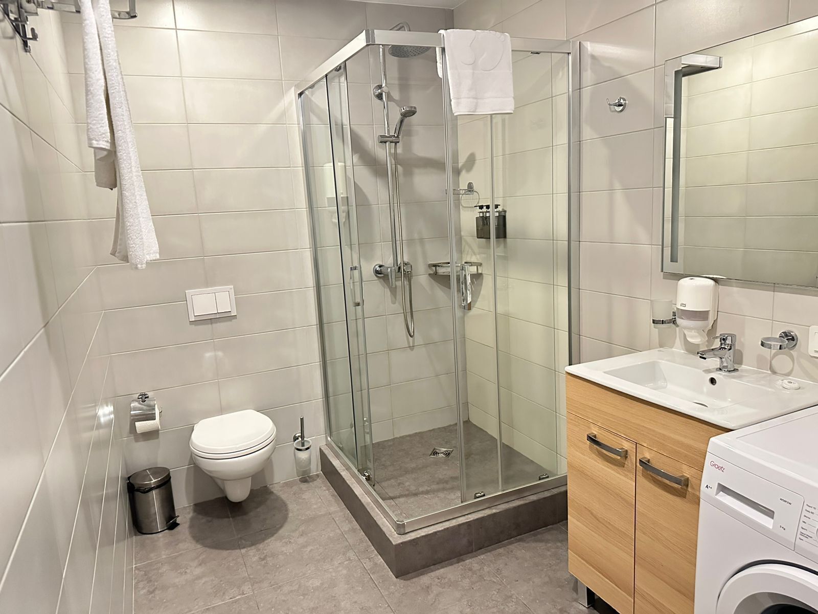 Een moderne badkamer met een douchecabine van glas, een toilet, een wastafel en een wasmachine.