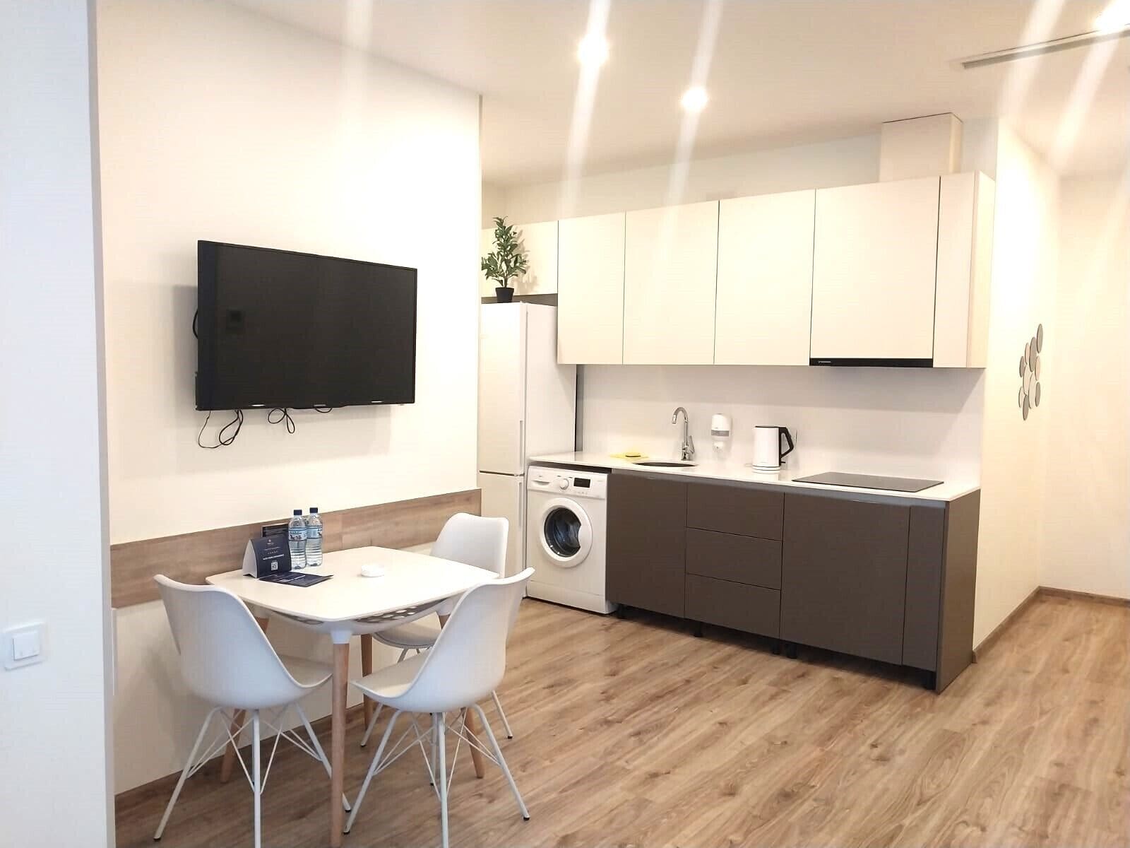 Eine kompakte Küche mit Waschmaschine, Spüle und flach an der Wand montiertem Fernseher.