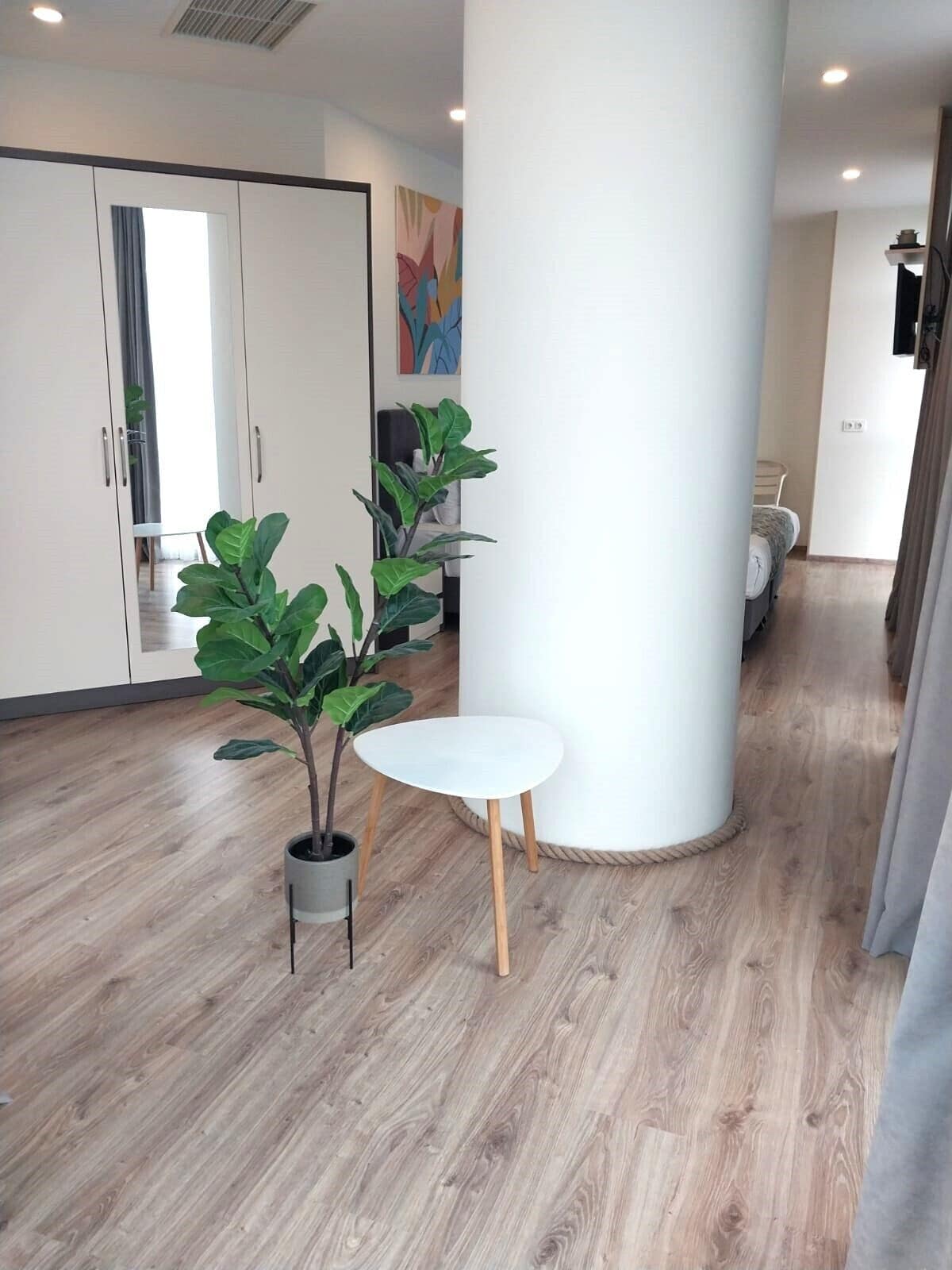 A modern interior with a wooden floor, a white pillar, a small white table, and two potted plants.
