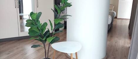 A modern interior with a wooden floor, a white pillar, a small white table, and two potted plants.