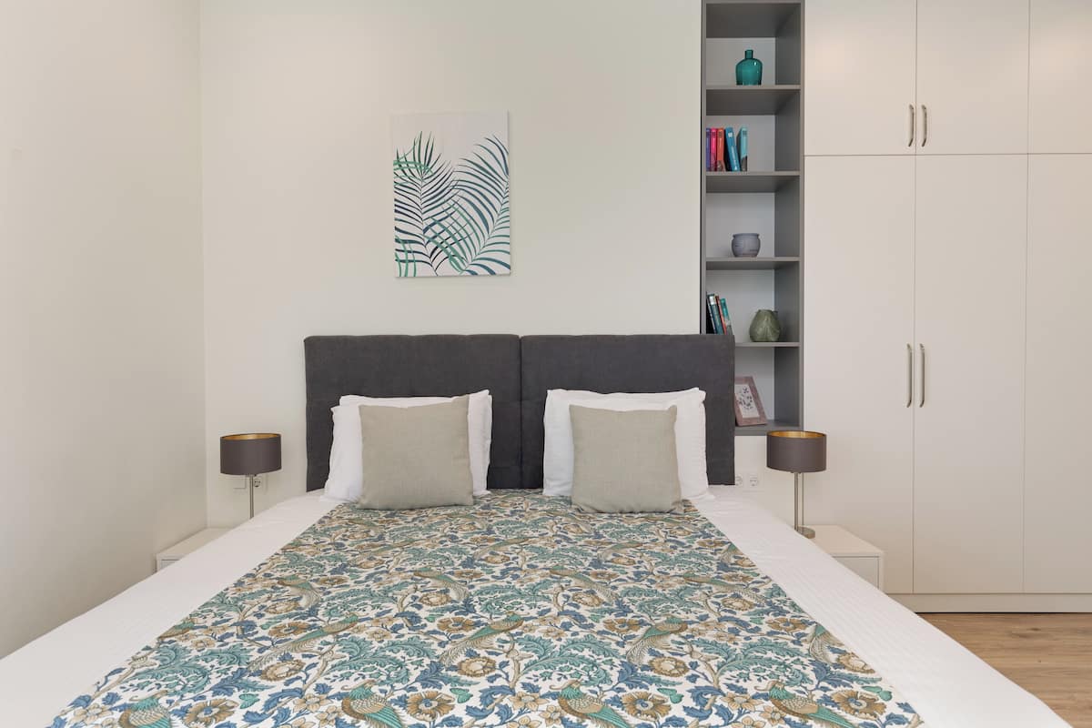 A bedroom with a bed, two bedside tables, a nightstand, a bookshelf, and a wardrobe.