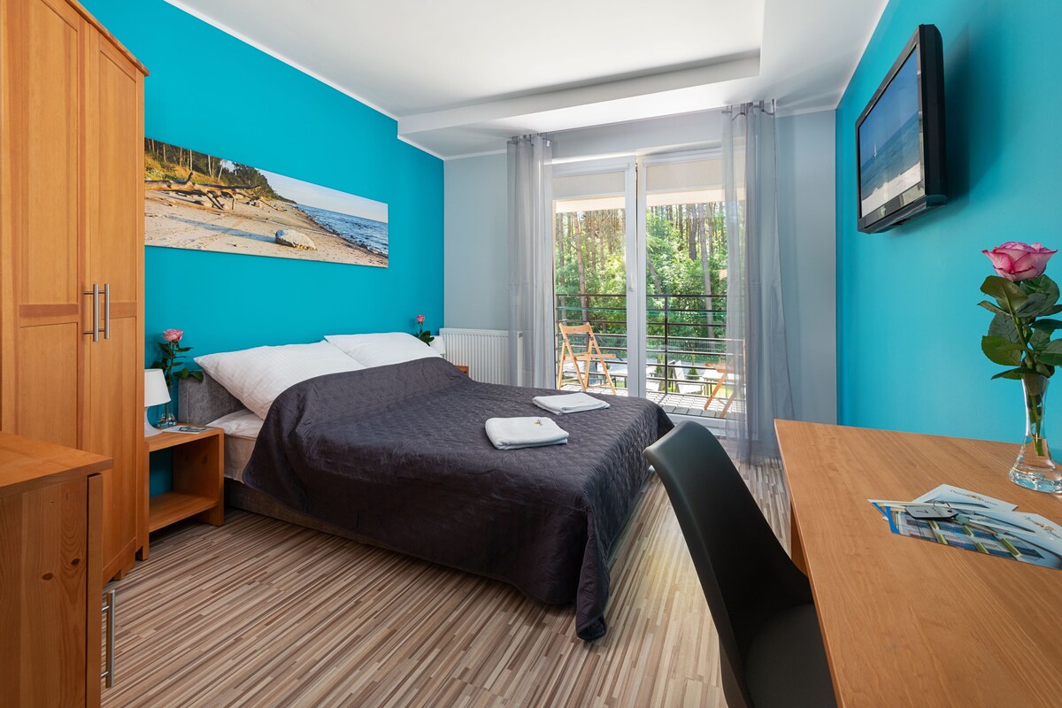 Ein Schlafzimmer mit Bett, einem Holzschrank, einem Schreibtisch mit Stuhl, einem Fenster mit Ausblick und einem Bild an der Wand.