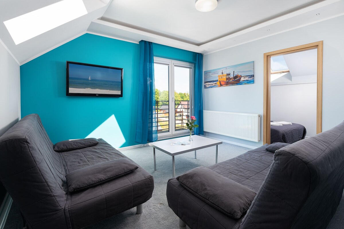 Ein modernes Wohnzimmer mit einer türkisblauen Akzentwand, einem großen Fenster mit blauen Vorhängen, einem Flachbildfernseher und einem Gemälde eines Bootes.