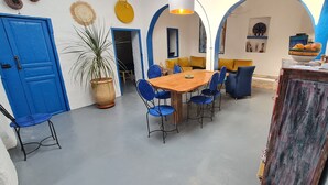 Uma área de refeições com uma mesa de madeira e cadeiras azuis, uma planta em vaso e uma porta azul.