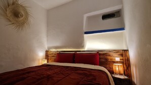 Quarto com cabeceira de madeira, almofadas vermelhas, colcha marrom e duas luminárias de mesa.