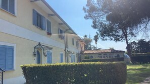 A two-story building with a light yellow facade, blue shutters, and a small garden area with neatly trimmed hedges. - Hotel Quadrifoglio by Mancini (Rome)