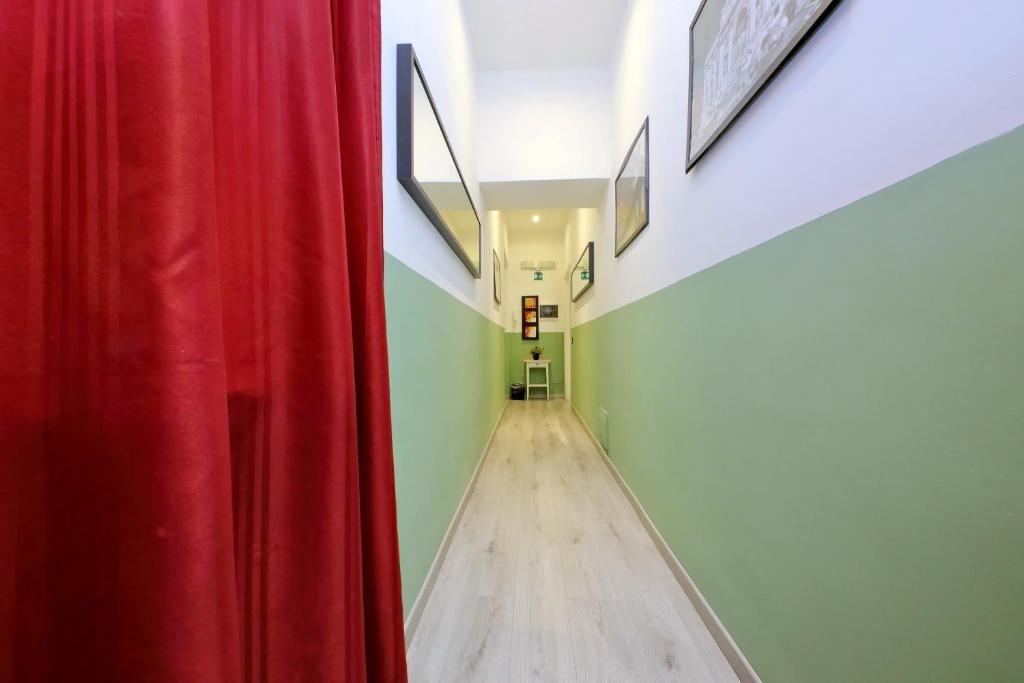 Un passadís amb una cortina vermella a l'esquerra, parets verdes i quadres amb marc a les parets.