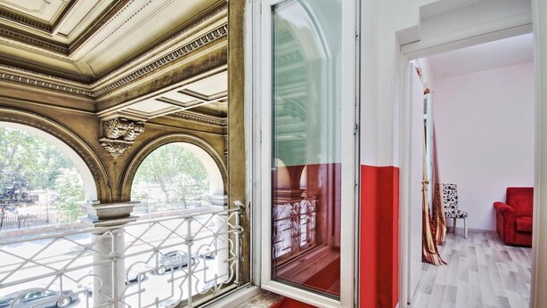 A room with a balcony, a red accent wall, and a view of the street. - Lucky Holiday Rooms (Rome)