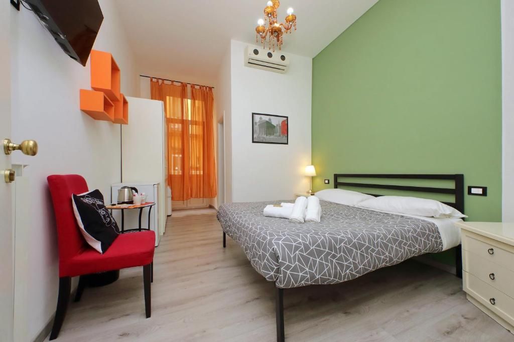 A hotel room with a bed, a chair, a bedside table, a lamp, and a picture on the wall.