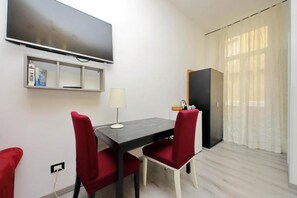 A small room with a flat-screen TV mounted on the wall, a dining table with two chairs, a lamp, and a wardrobe. - Lucky Holiday Rooms (Rome)