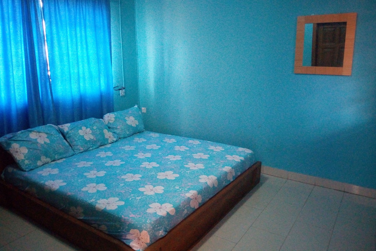 A bedroom with a bed, curtains, a wall-mounted picture frame, and a tiled floor.