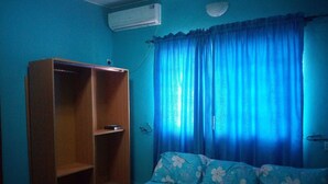 Una habitación con cama, armario y ventana con cortinas azules.