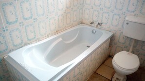 Un baño con bañera, inodoro y azulejos estampados.