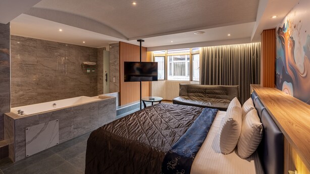 A modern hotel room with a large bed, a separate bathroom, a flat-screen TV, and a large window with curtains. - King & Princess Motel-Rende (Tainan)