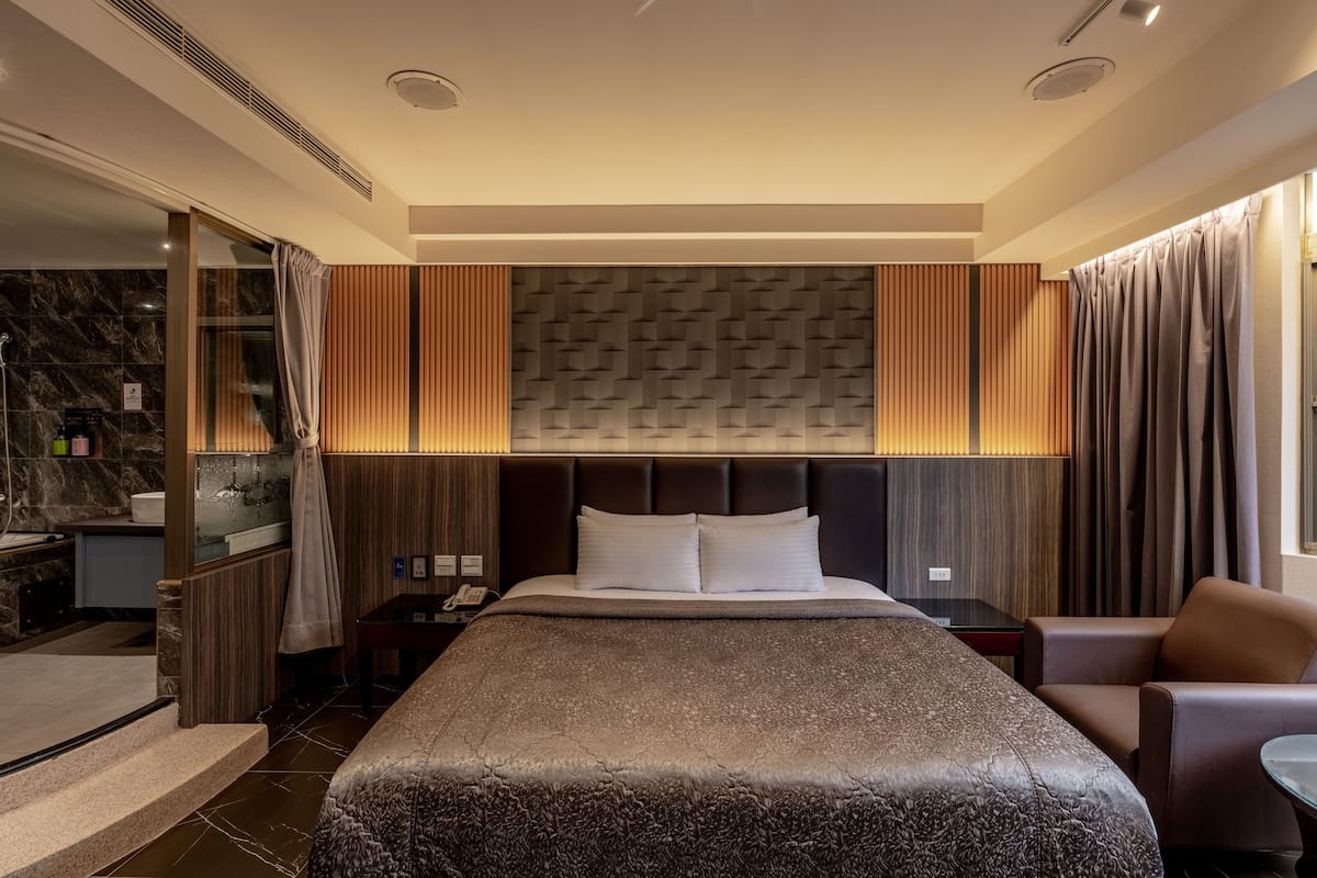 A modern hotel room with a large bed, a desk, a chair, and a bathroom visible through an open door.