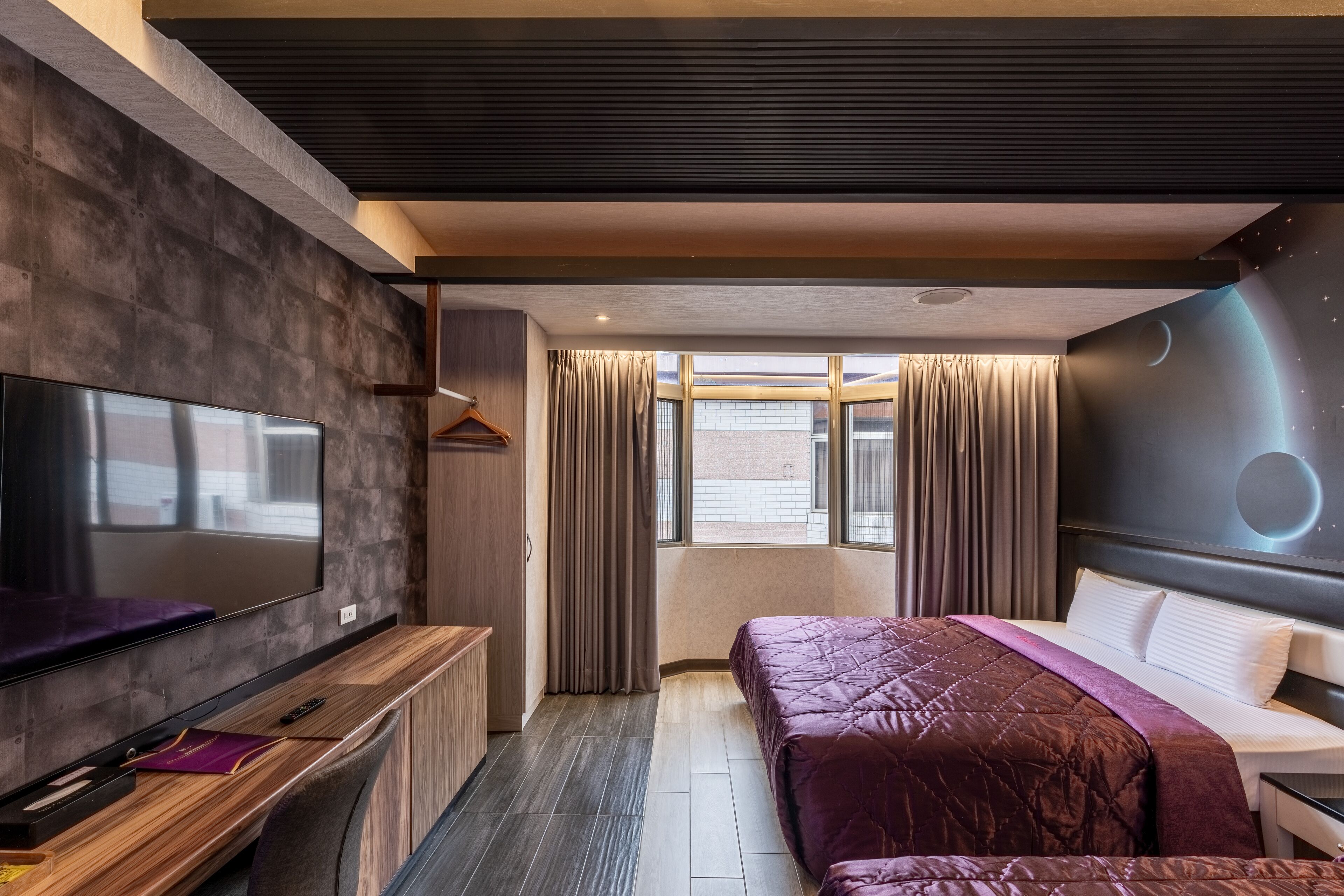 Een moderne hotelkamer met een grote flatscreen-tv, een houten console tafel, een bed met een paars quiltje en uitzicht op de stad door grote ramen.