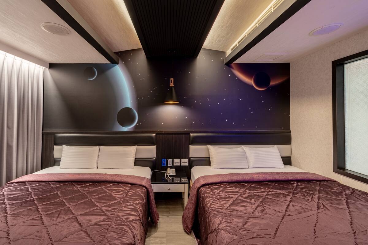 A hotel room with a bed, two bedside tables, a nightstand, and a wall mural of space.