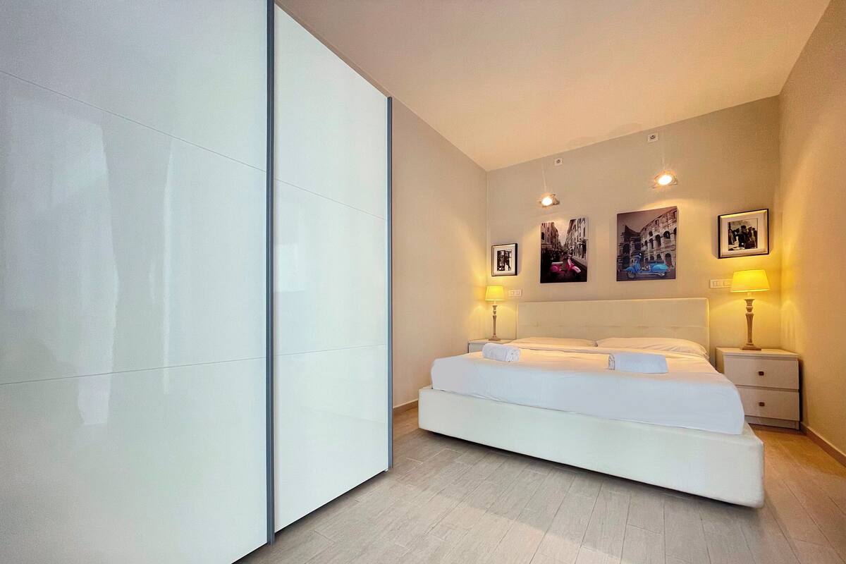 A modern bedroom with a large bed, two bedside tables with lamps, and three framed pictures on the wall.