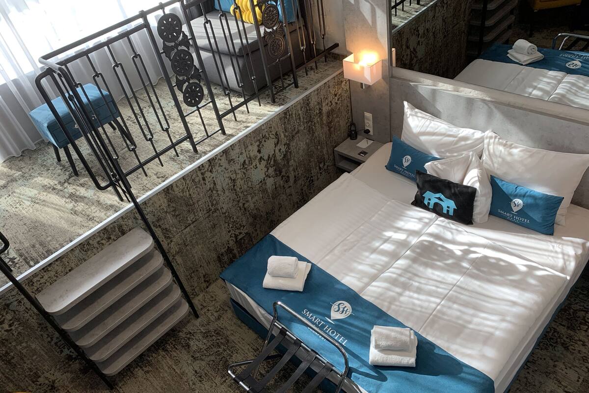 A hotel room with a bed, a nightstand, a lamp, a chair, and a view of a staircase.