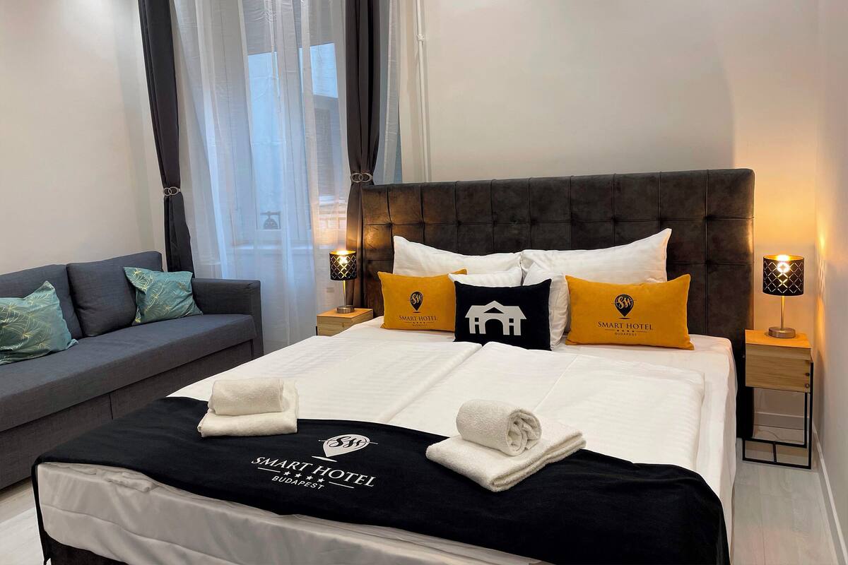 A hotel room with a large bed, a grey sofa, and two bedside tables with lamps.