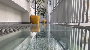 A modern indoor corridor with a glass floor reflecting the surroundings, including a yellow planter and a potted plant. -  Smart Hotel Budapest (Budapest)
