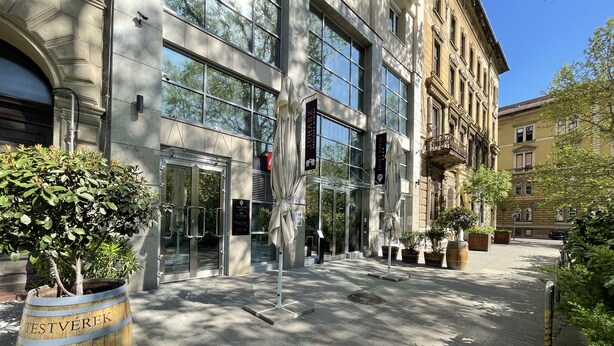 A building with large glass windows, a wooden barrel labeled "Testvereik Brewery" in the foreground, and a clear blue sky. -  Smart Hotel Budapest (Budapest)