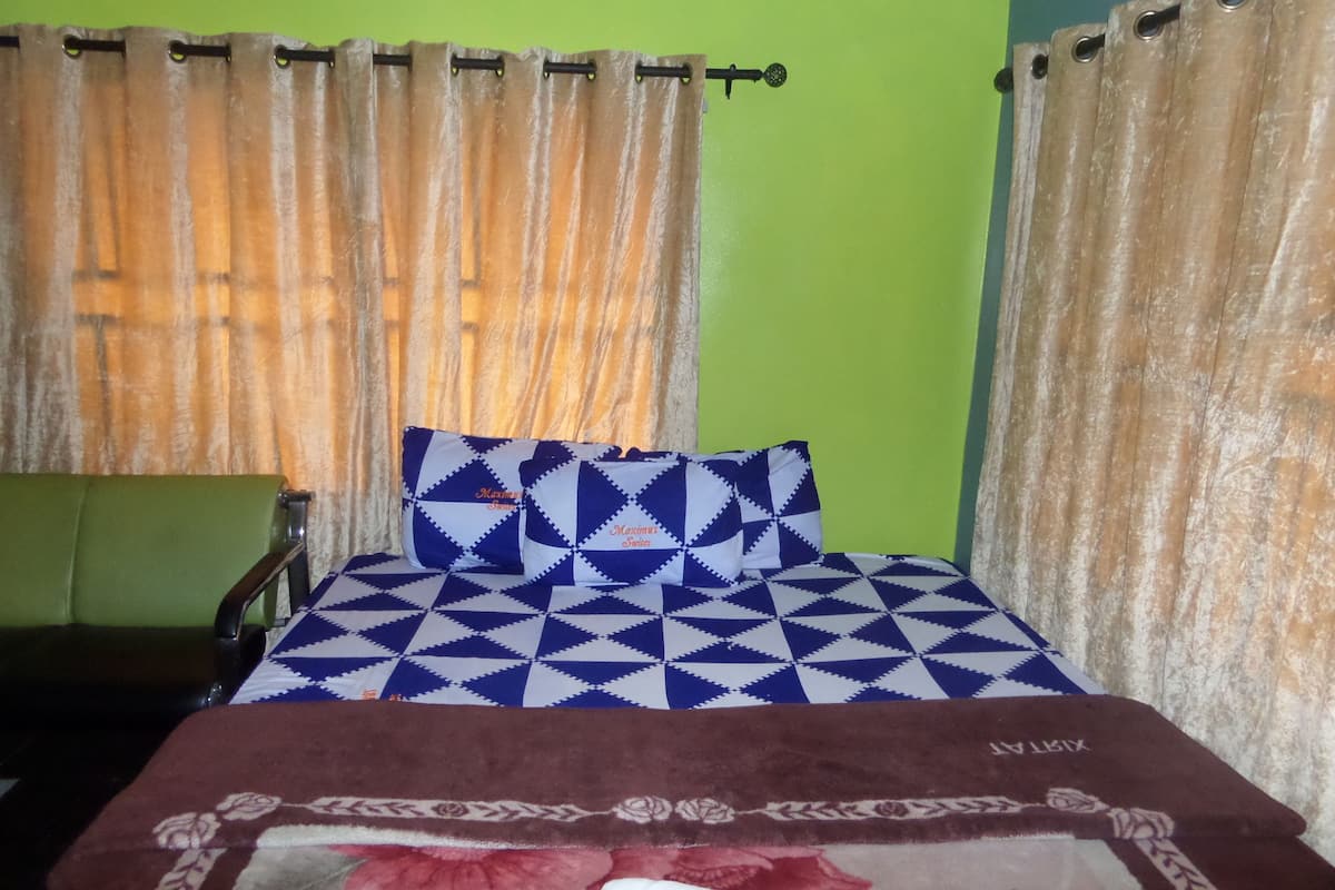 A bed with a patterned bedspread and pillows, a brown throw blanket, and a green wall.