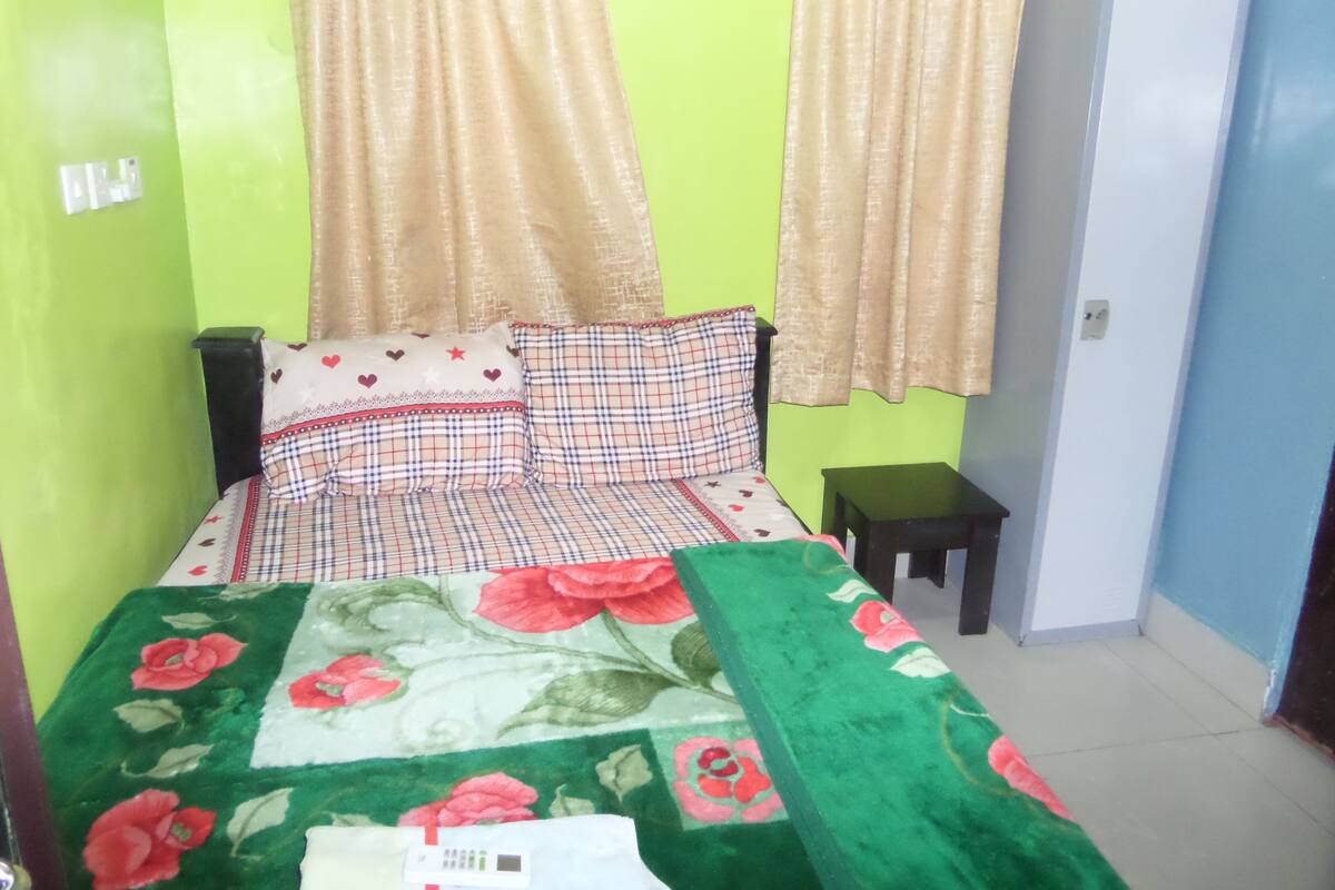 A room with a bed, green walls, a small table, and a door.
