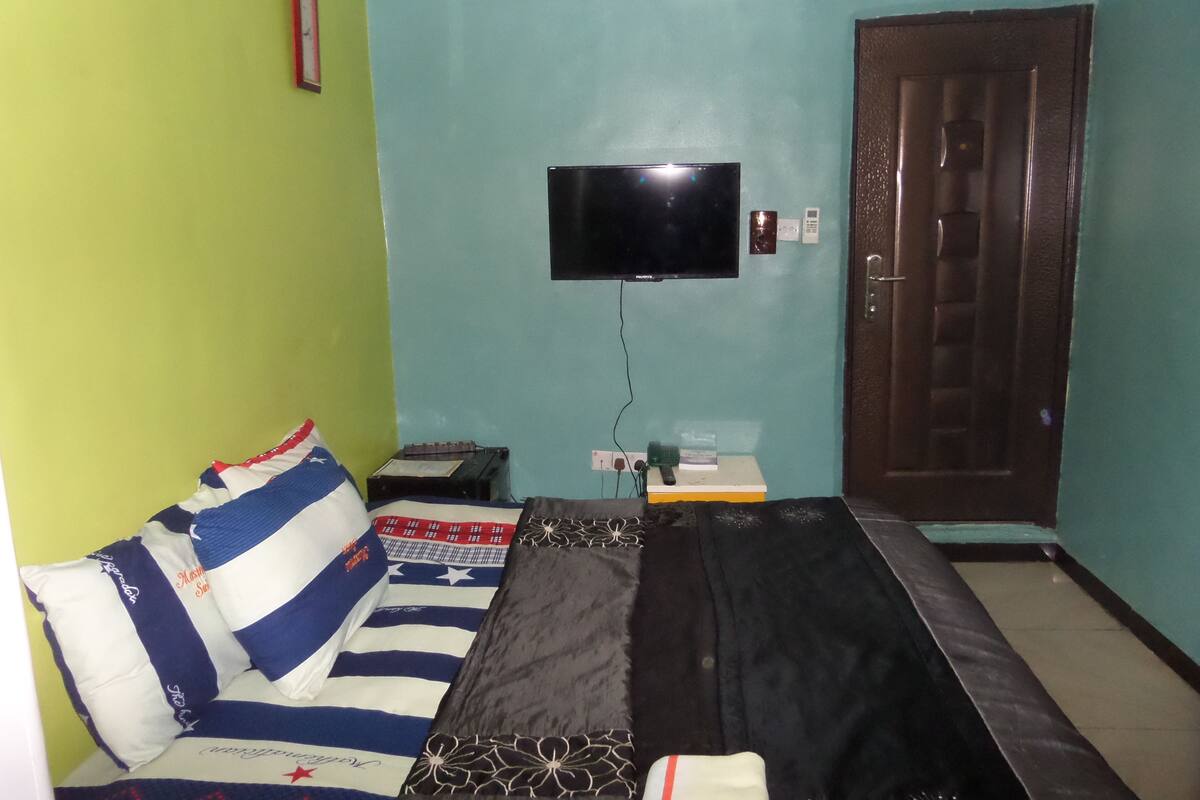 A room with a sofa, a TV mounted on the wall, a small table with a remote, and a door.