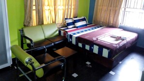 A room with a bed, a green sofa, a small table, and a chair. - Maximus Suites (Lagos)