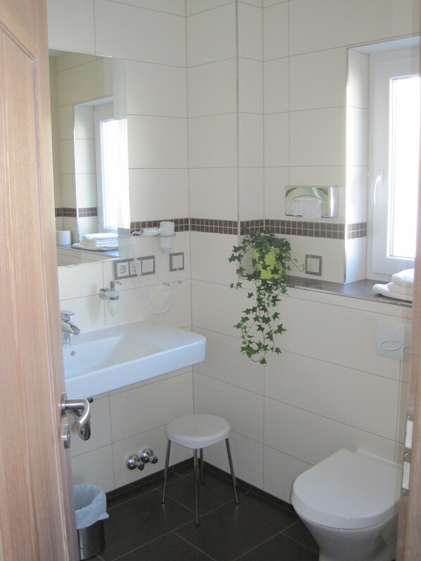 A bathroom with a white sink, a toilet, and a small stool. - Landhotel Velte (Neu-Anspach)