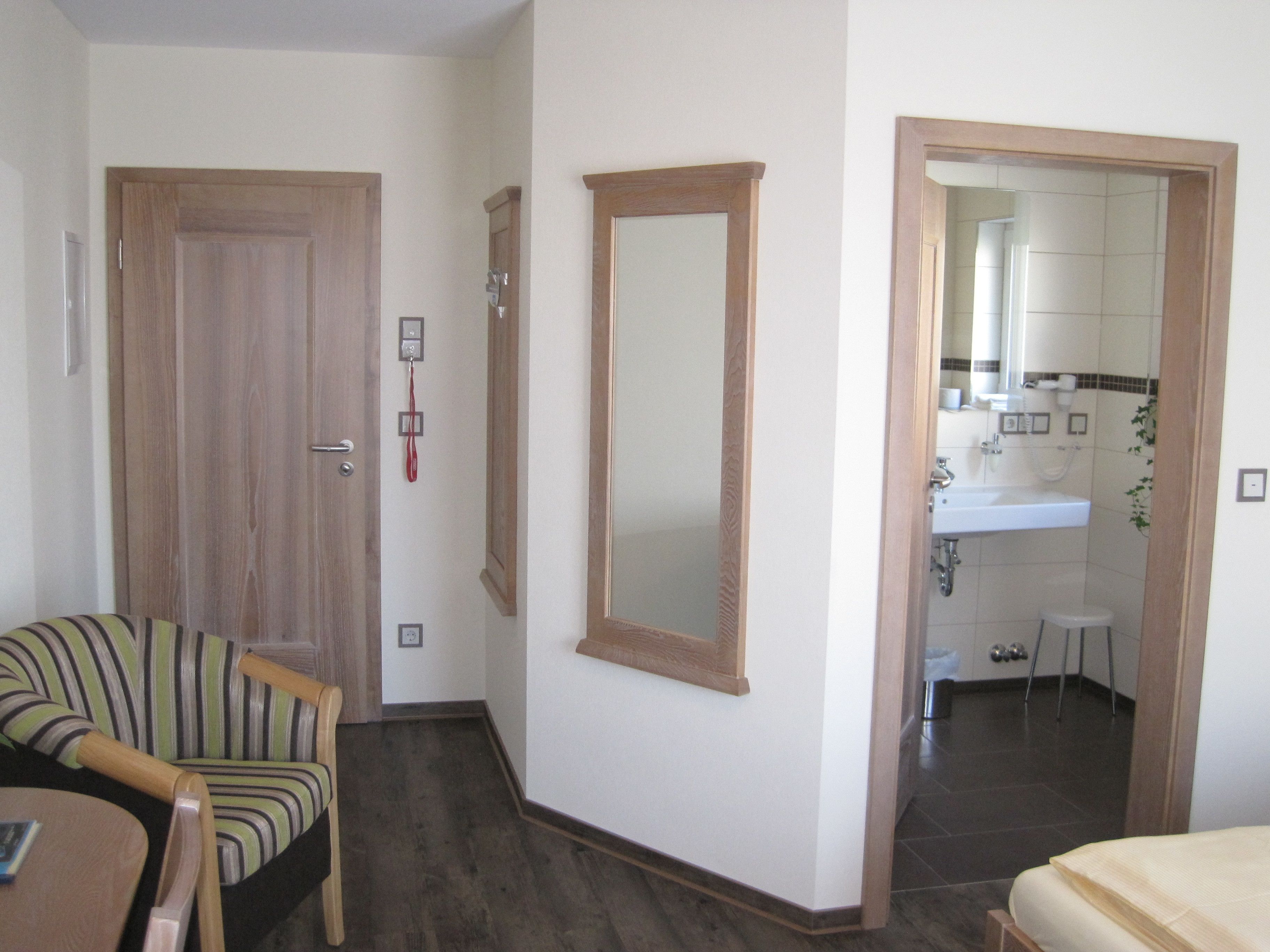 A hotel room with a wooden door, a mirror, a small stool, and a bed.